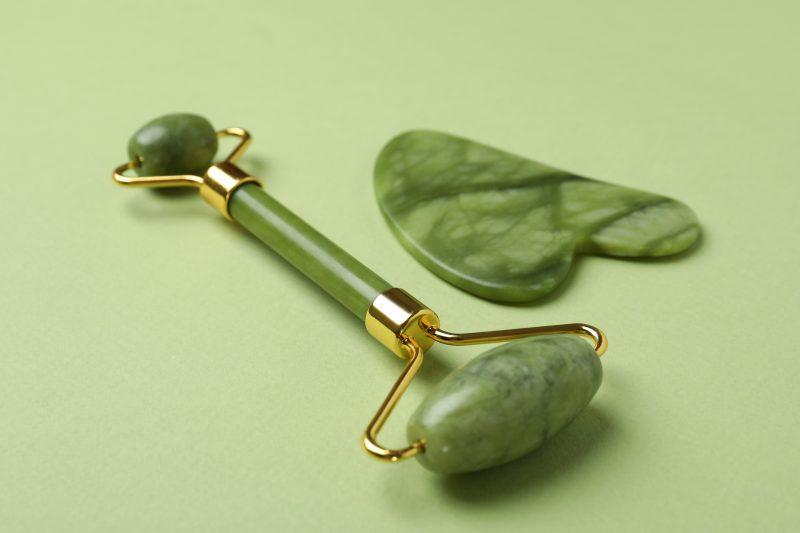 face roller and gua sha on green background